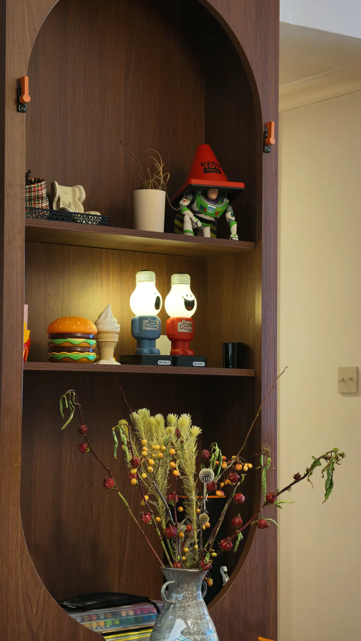 Arched dark timber display niche with shelves holding figures, flowers and small objects.