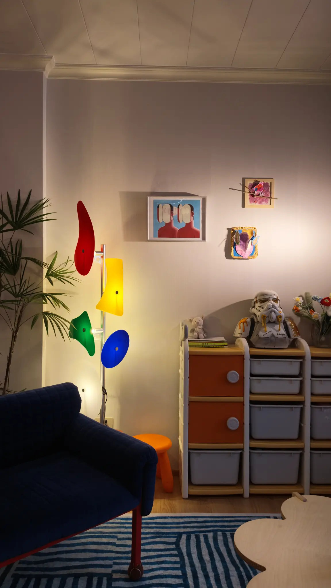 Blue sofa, colourful floor lamp, artworks and storage drawers in a living space.